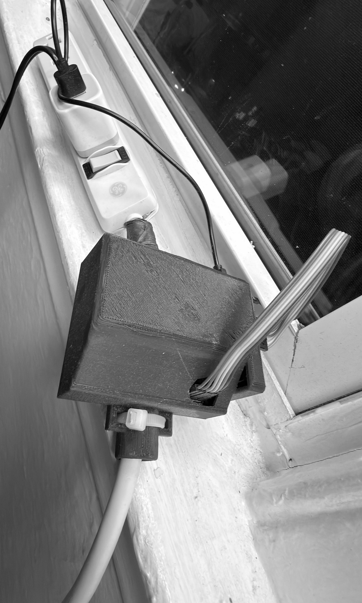 White extension cord installed with a dark 3D-printed ESP32 and relay housing, cord clamp, and parallel ribbon wiring